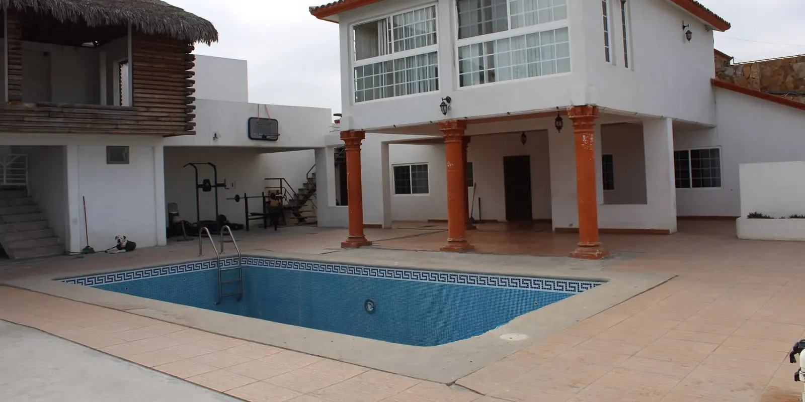Empty courtyard pool outside a two-storey white residence with orange columns and a covered terrace