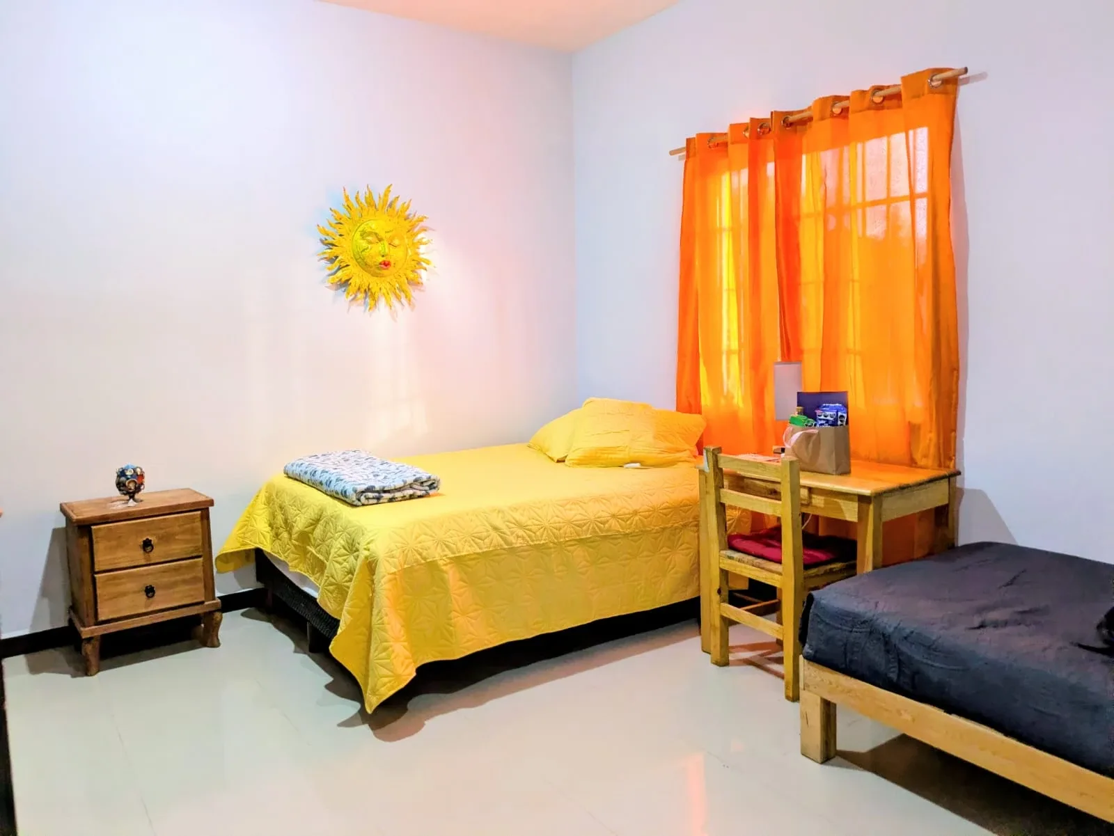 Bedroom with yellow and dark bedding, a wooden desk and orange curtains