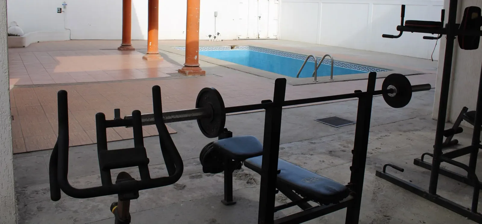Exercise equipment and a weight bench beside the courtyard swimming pool