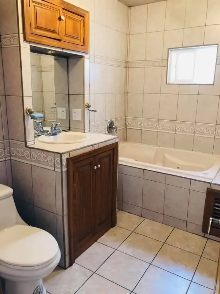 Empty tiled bathroom with bathtub, sink, mirror, wooden cupboards and toilet