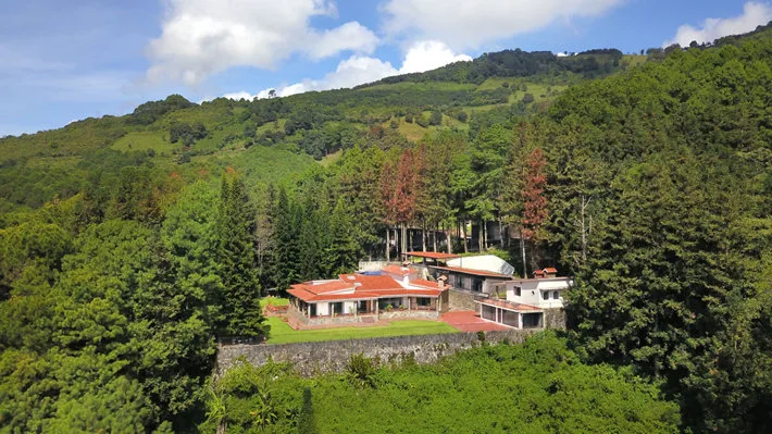 Hillside campus buildings with red roofs surrounded by wooded grounds