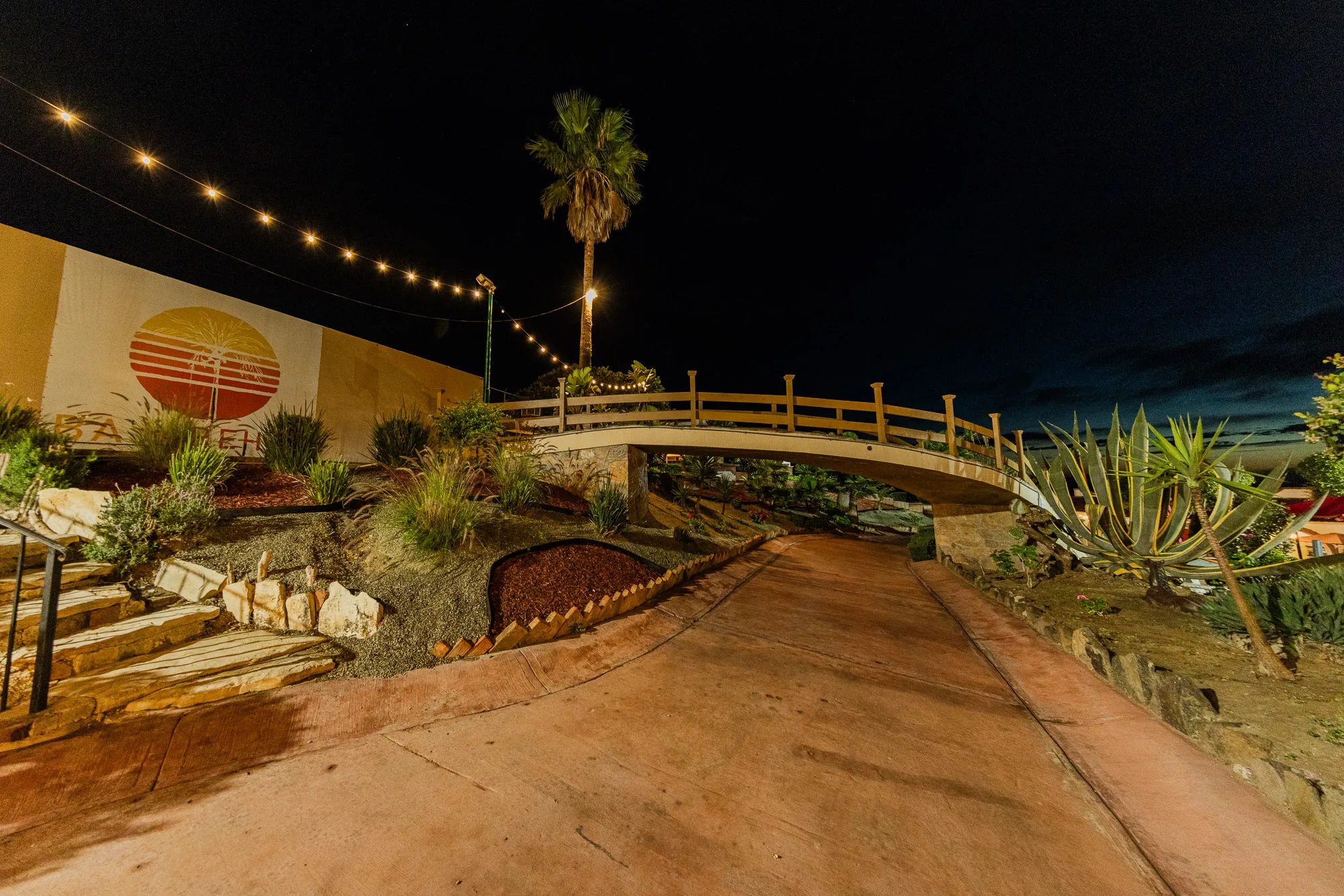 Illuminated garden paths and wooden bridge at Baja Rehab after dark