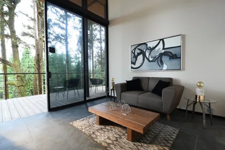 Cabin living room with sofa, coffee table, large windows and a forest-facing balcony