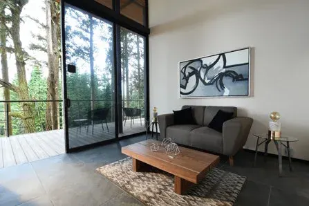 Cabin living room with sofa, coffee table, large windows and a forest-facing balcony